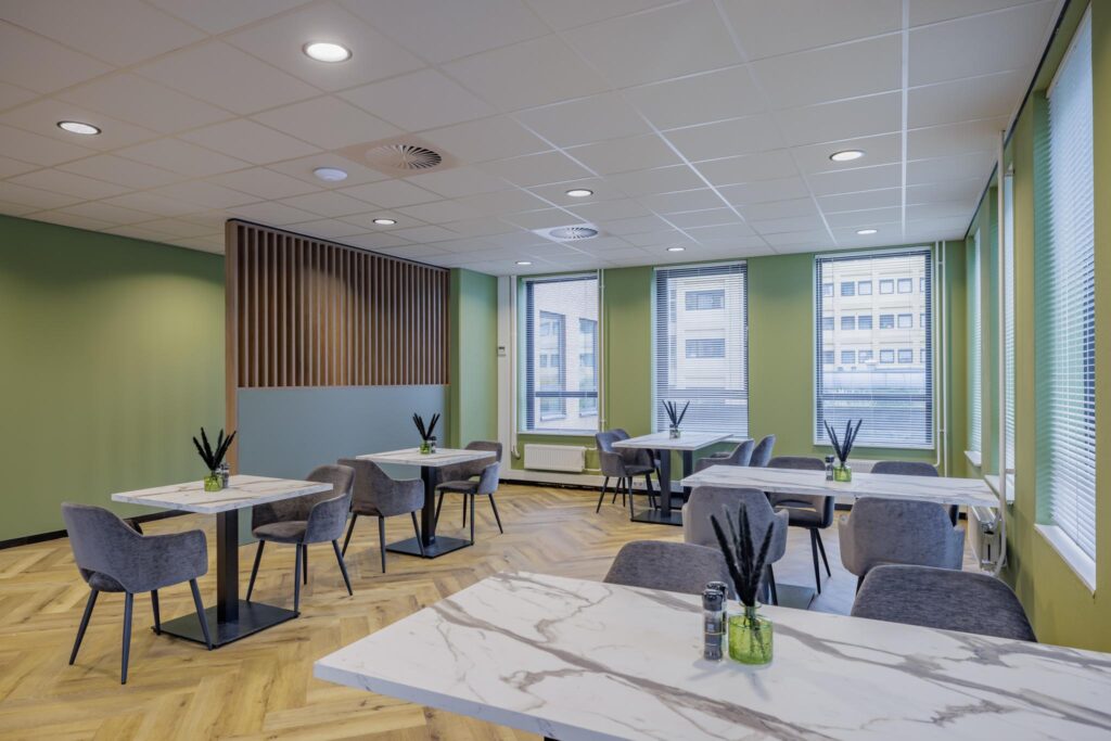 Modern cafeteria with marble tables, grey chairs, and green walls located on Hiridostraat.